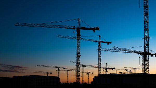 The silhouette of tower cranes on a construction site at sunset.
