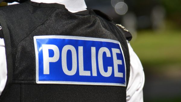 The back of a police officer in uniform displaying a blue 'police' sign