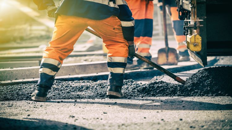 Shot of a worker's feet as they shovel tarmac