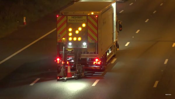 Balfour Beatty's automatic cone laying machine sets cones out on a dark road with a large flashing orange arrow sign at the rear to warn traffic