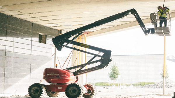 A red MEWP lifts a worker in yellow hi-vis to the concrete ceiling of a building.