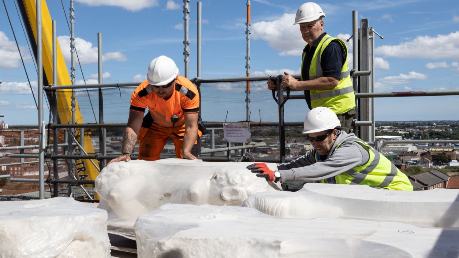 Three workers in hi-vis jackets and hard hats manoeuvre some of the 12 stone putties into place. Hobson & Porter lifted the stones into place at Hull's Guildhall by crane.