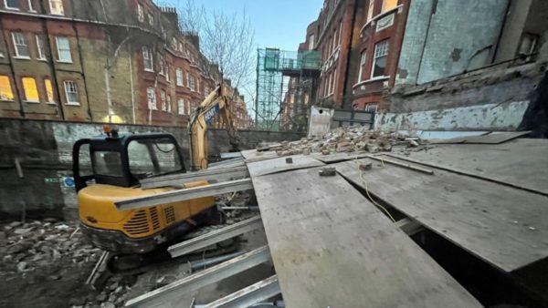 A construction site with rubble, a digger and houses at the back.