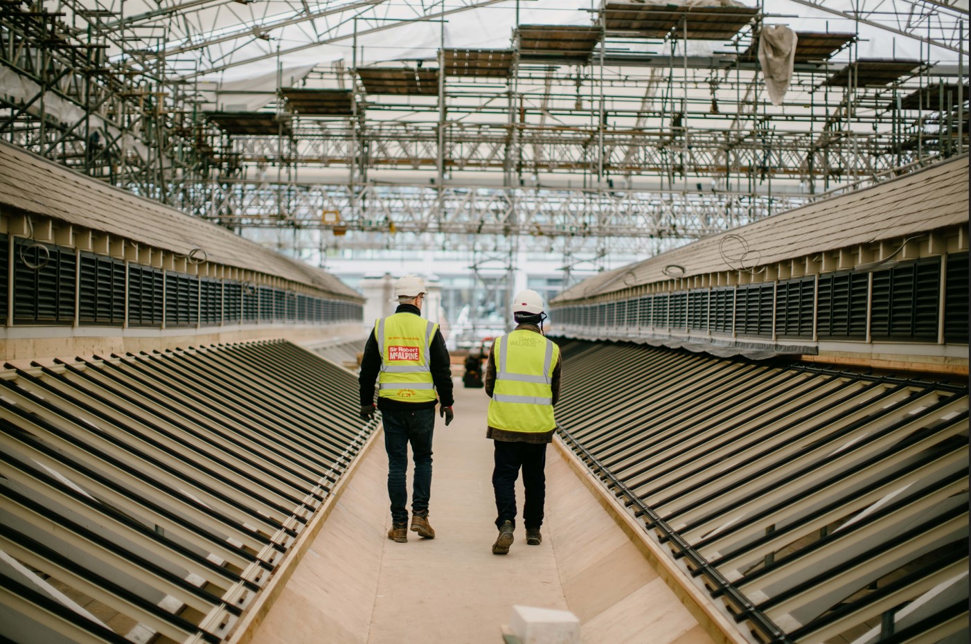 Two people with high-vis jackets and hard helmets walking on a construction site.