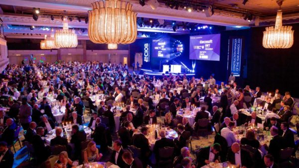 A fancy indoors venue with people seating at tables and a stage at the back.