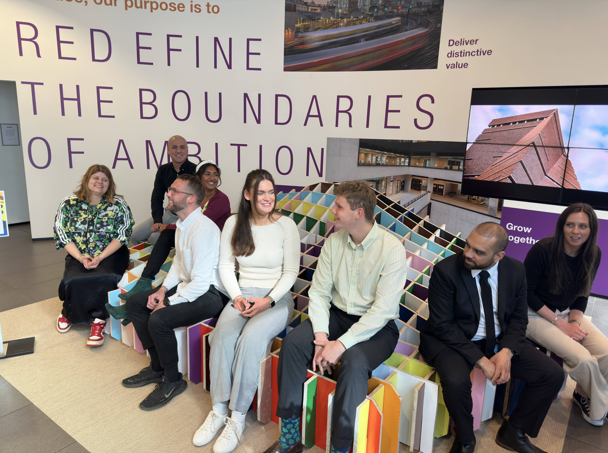 Pride Month - A group of people seating on a colourful installation. 