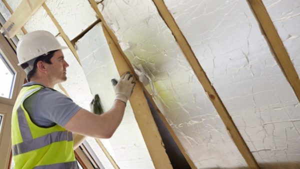 A male builder fitting insulation into roof of new home.