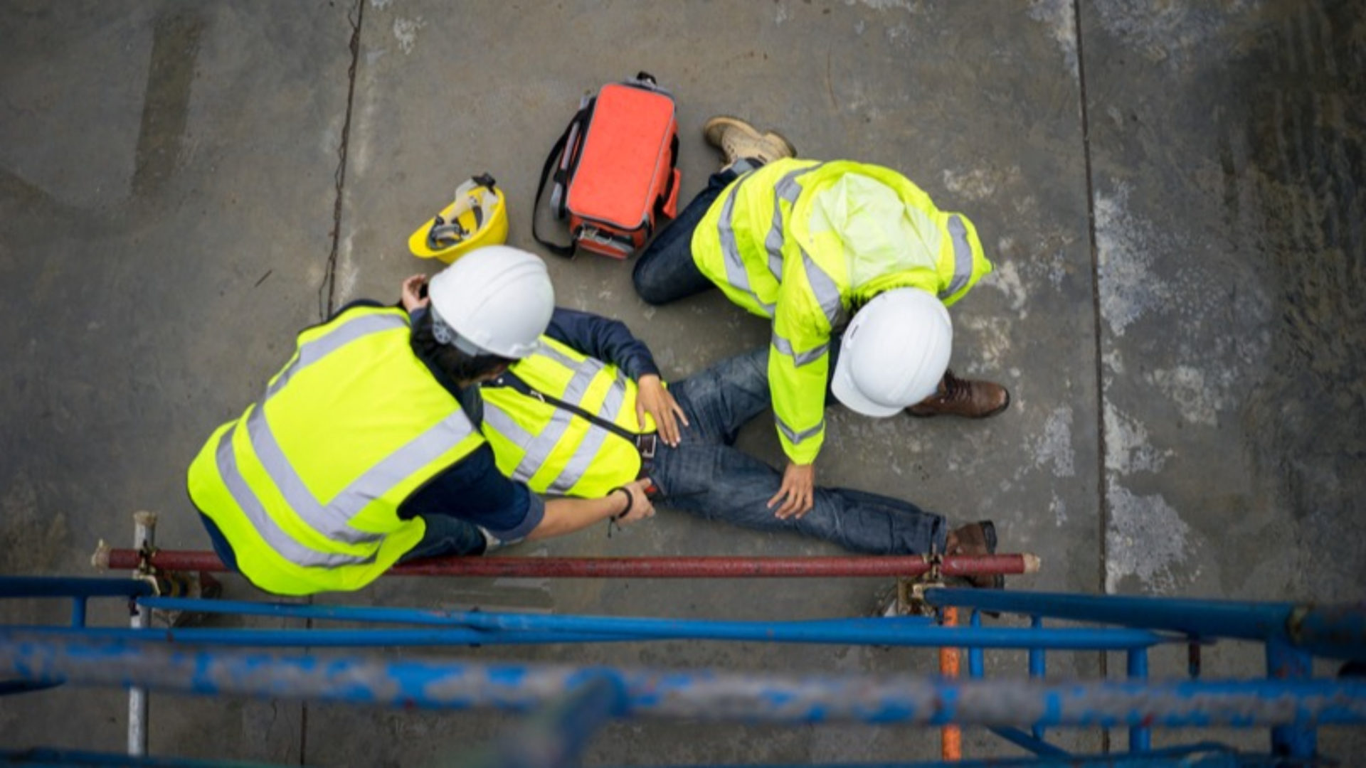 HSE construction fatalities - Two workers assisting a third one who is on the floor injured. They are all wearing high-vis jackets.