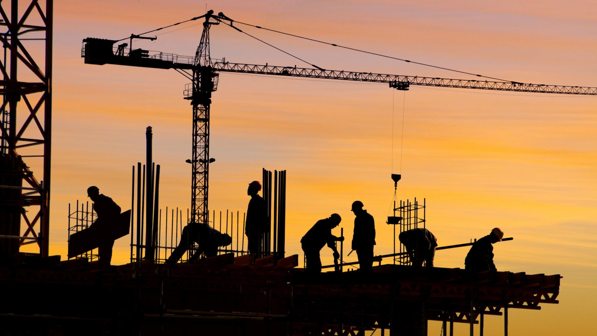 Silhouette of people working on a construction site at sunset