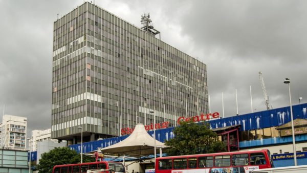 View of a shopping centre and big office block. There are also two-decker buses.