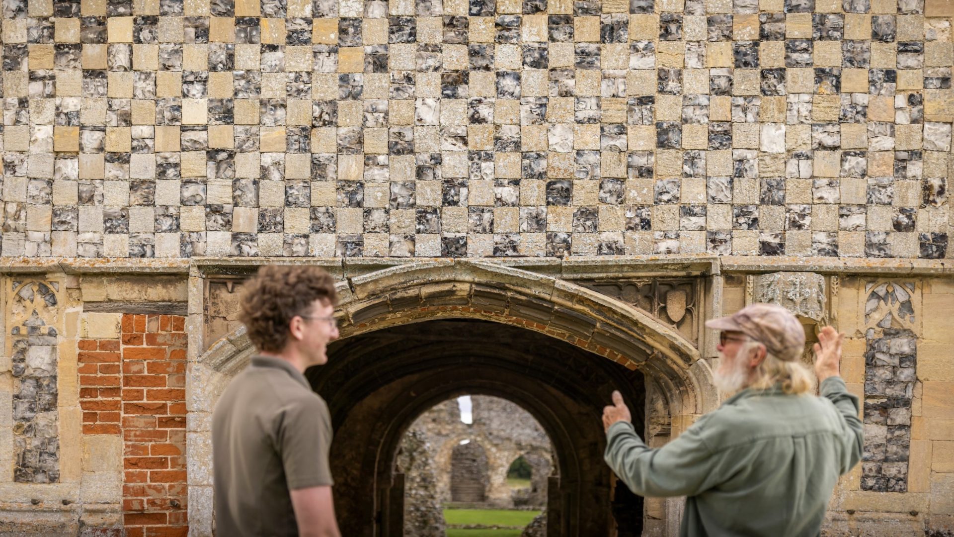 Two people facing a stone building with an arch.