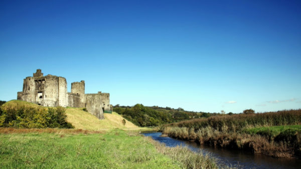 View of a field with a river and some castle ruins.