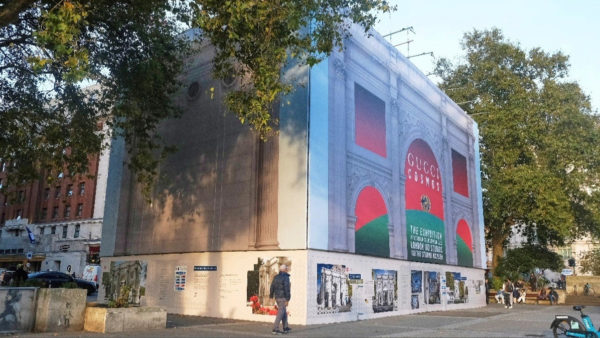 A scaffolding structure with a wrap in a square with people walking around it.