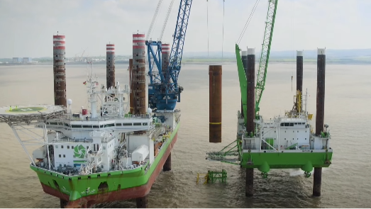 Big cranes and offshore platforms and a big tube being lowered down.