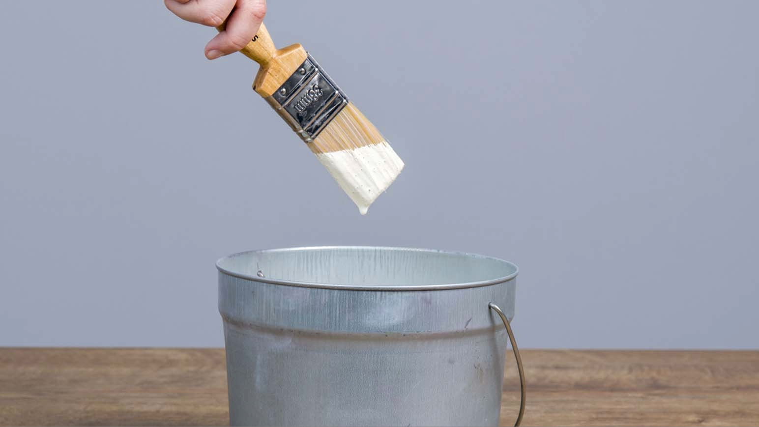 A hand with a brush with paint and a bucket.