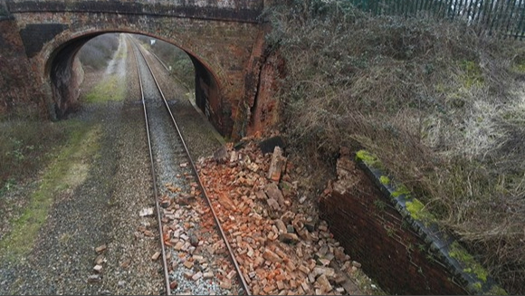 View of train tracks with debris on them and a bridge in the background.