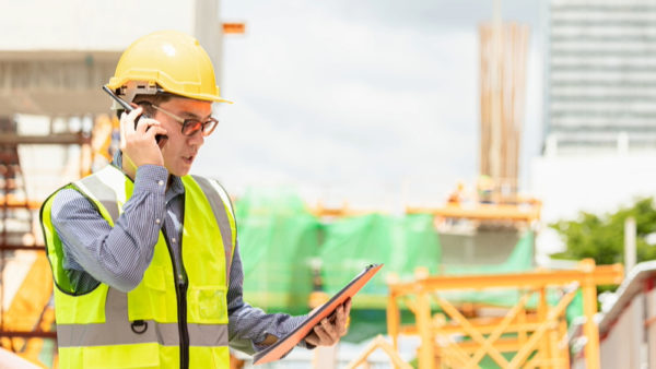 A construction worker with hard hat and high-vis jacket with a clipboard and talking on a walkie-talkie -- Variation claims