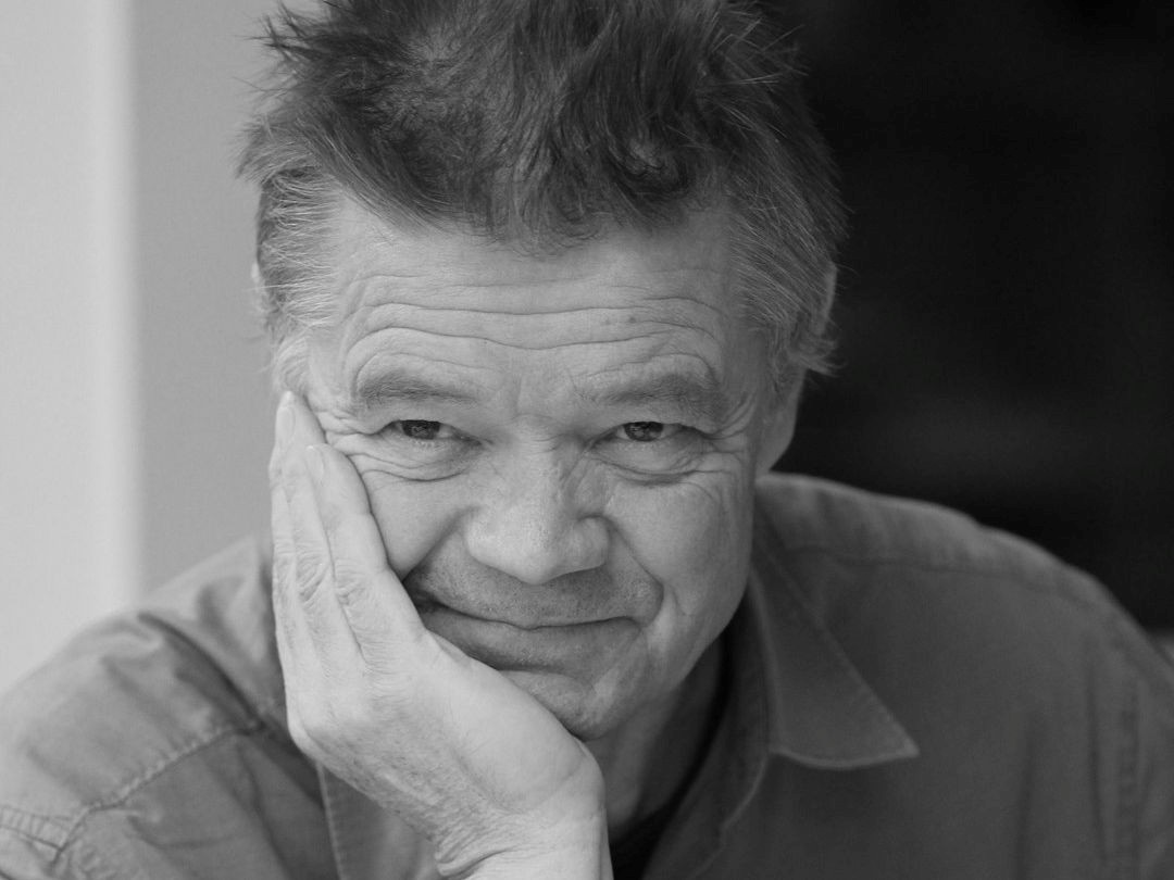 Black and white mugshot of Peter Clegg holding his head on his palm. He has been awarded an OBE for his services to architecture