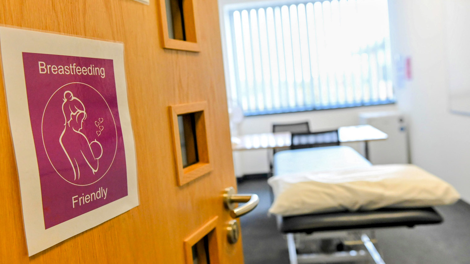 A room with the door open and a bed in the middle. There's a sign on the door which says 'breastfeeding friendly'