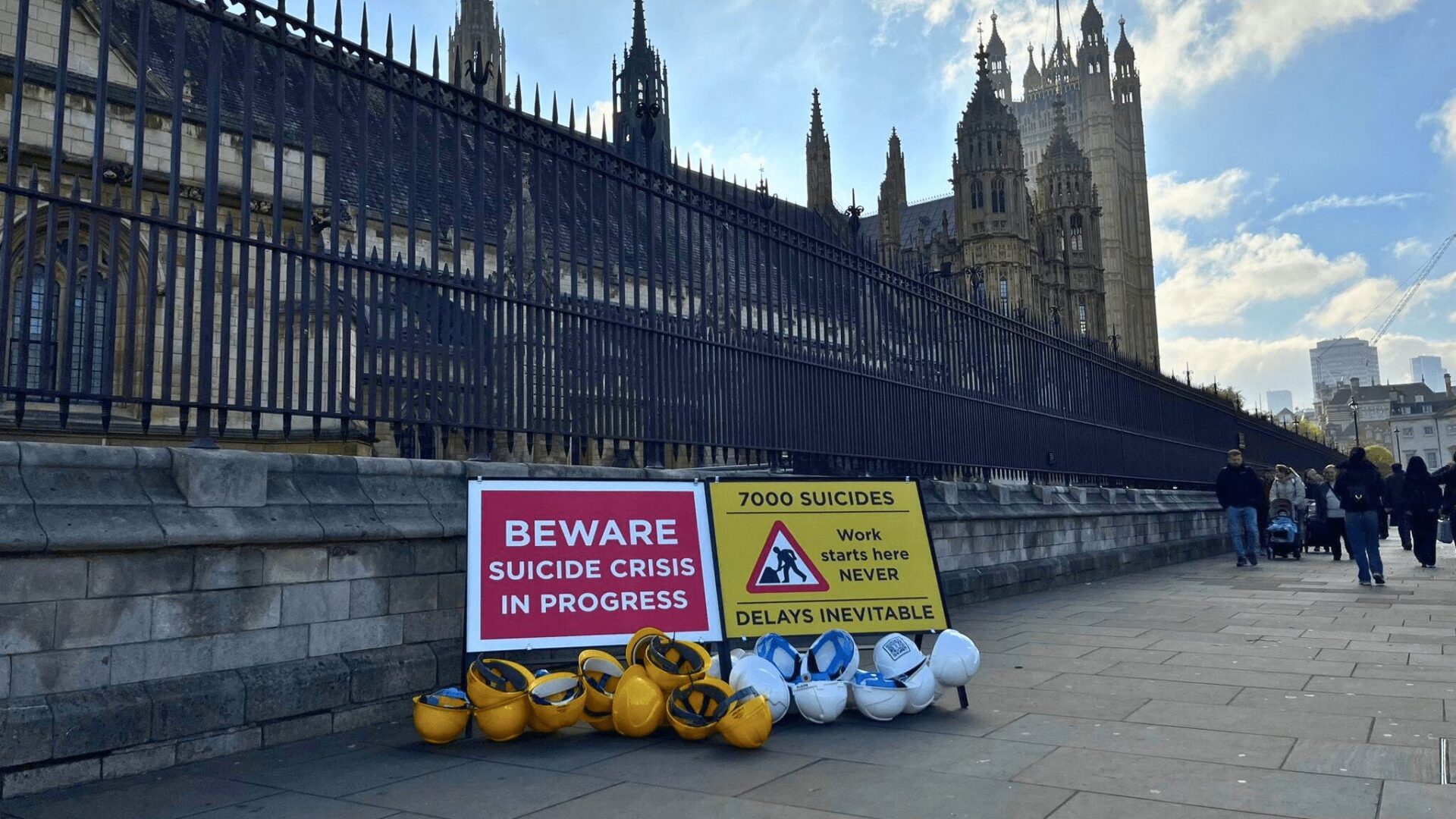 Two construction signs outside the UK Parliament that say 'beware, suicide crisis in progress' and '7,000 suicides. Work starts here NEVER. Delays inevitable'.