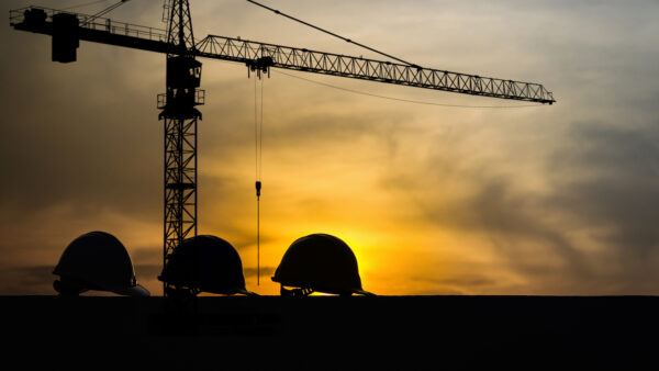 Silhouette of three hard hats against a crane background