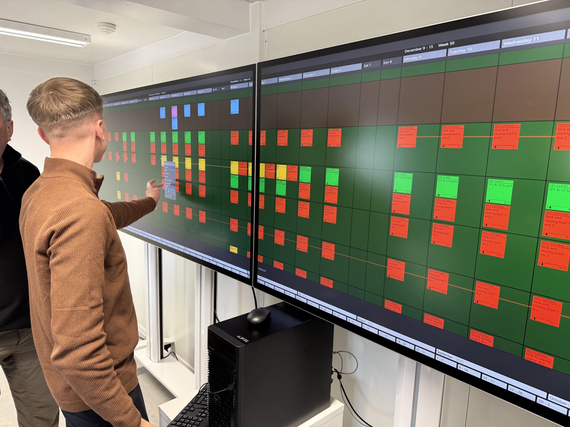 A big, long monitor with green and red squares on it. There's a man pointing at it - Digital Construction Awards 2025 - Willmott Dixon in partnership with Nialli and Ascentae