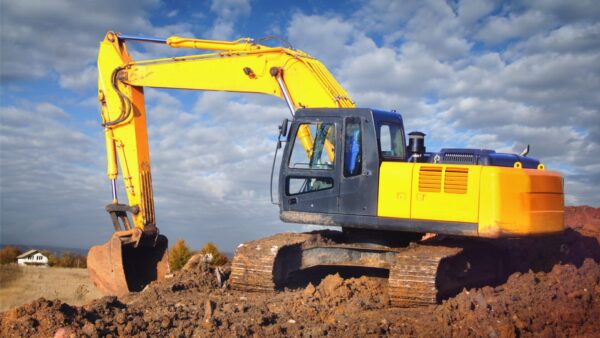 A yellow excavator moving earth on a field - HSE has issued an excavator safety warning.
