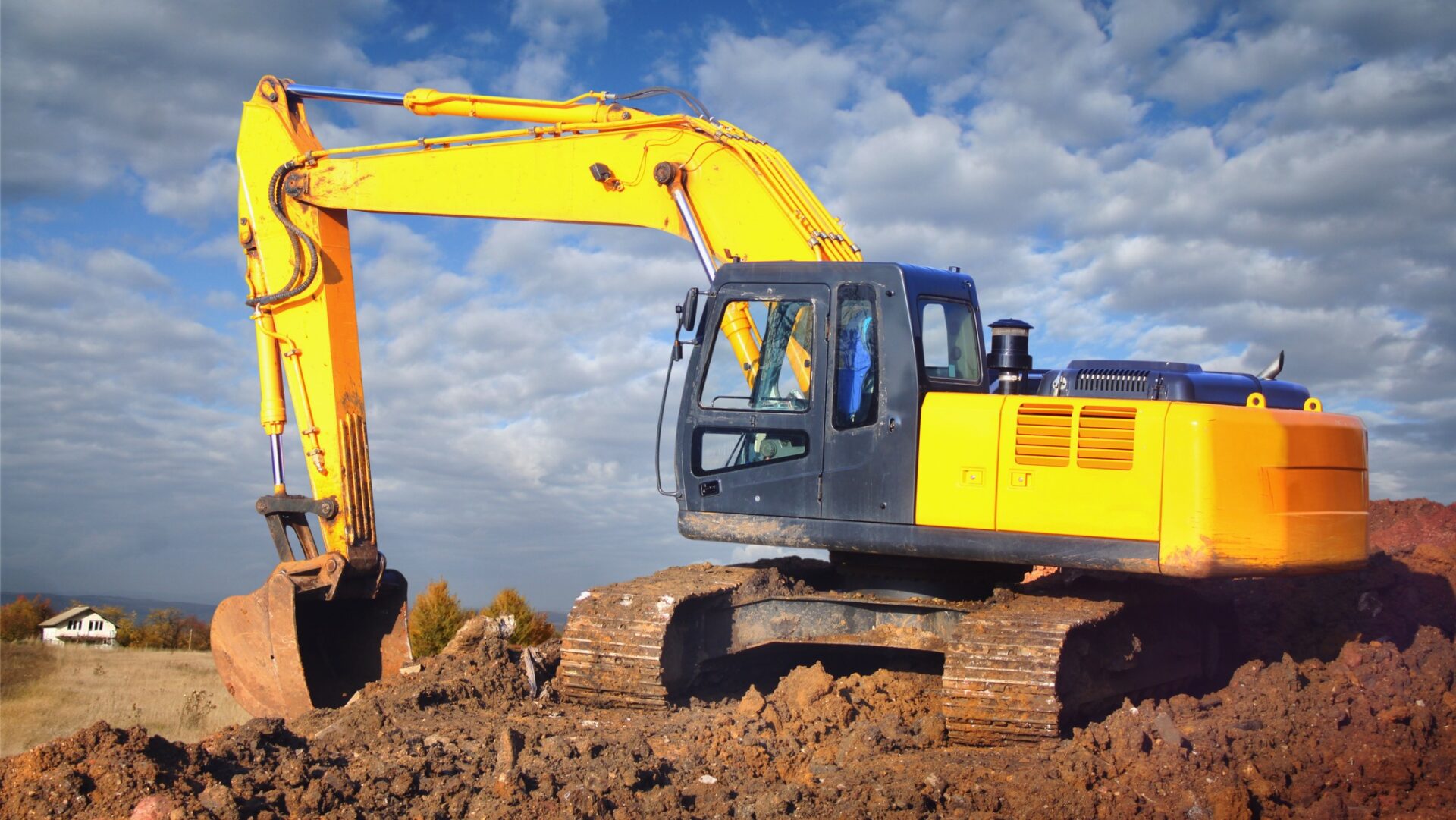 A yellow excavator moving earth on a field - HSE has issued an excavator safety warning.