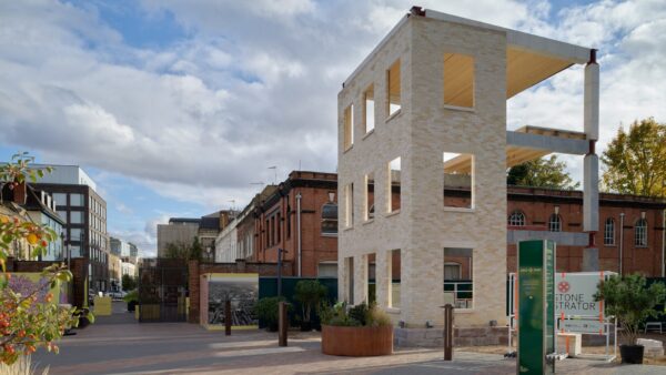 A three-storey structure made of light-coloured bricks with other buildings in the background